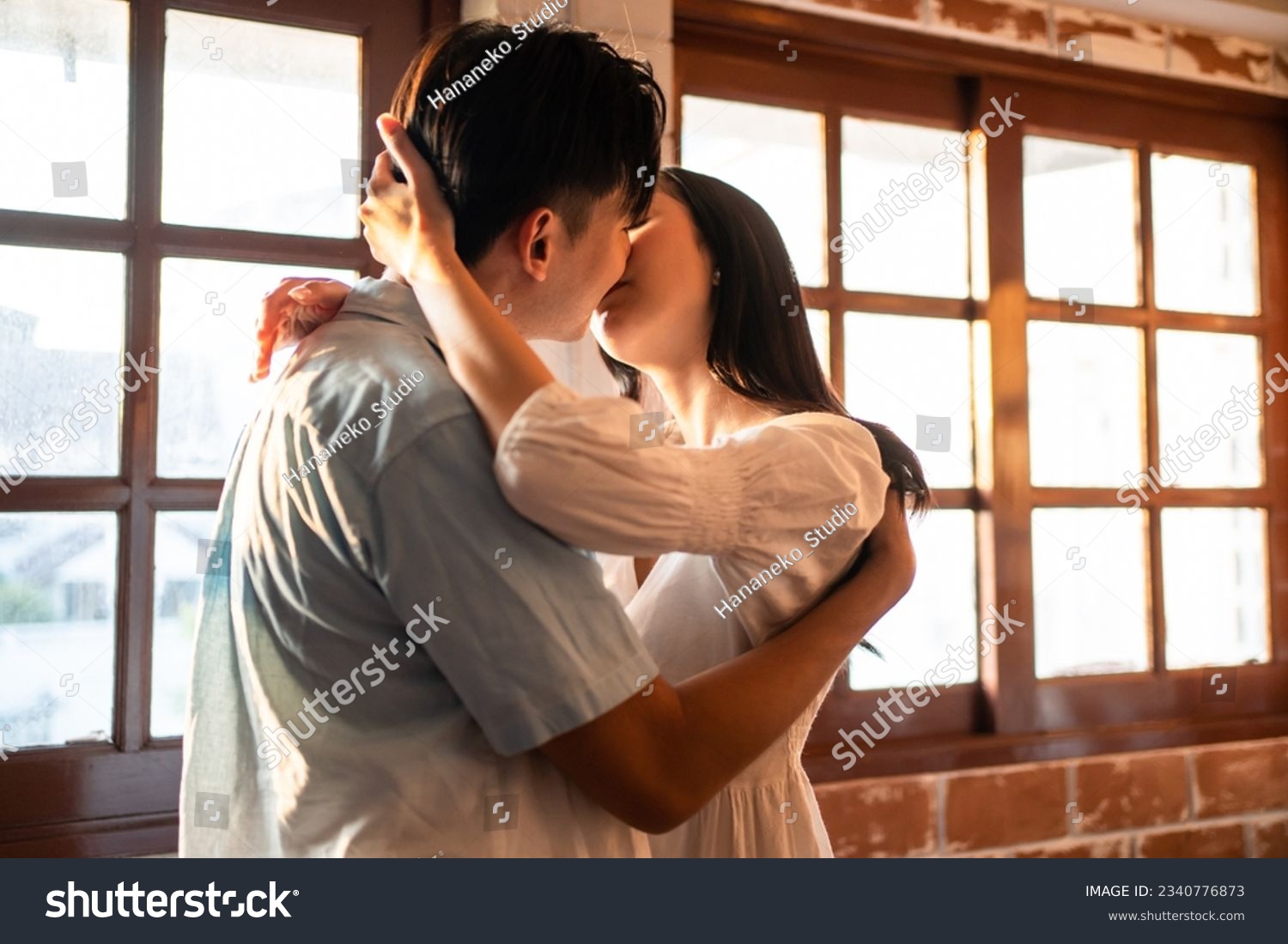 Asian young man and woman kissing each other in living room at home. Attractive romantic new marriage couple male and female spend time celebrate anniversary and valentine's day together in house. #2340776873