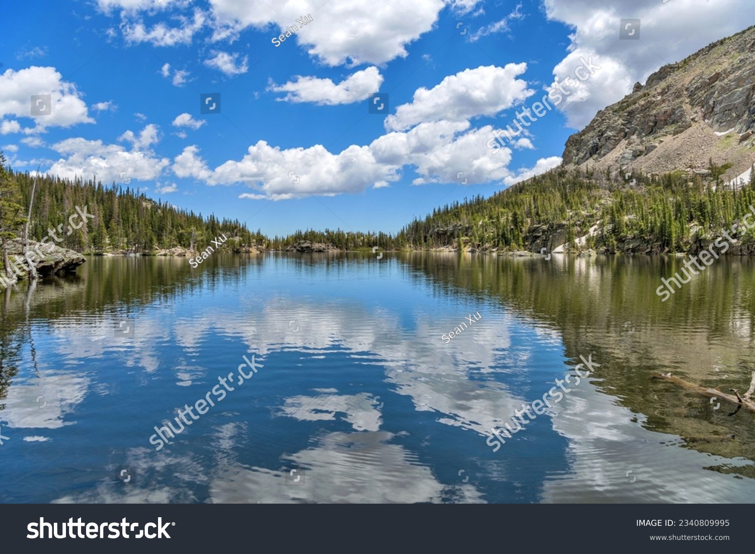 The Loch - A summer day view of blue sky and white clouds reflecting in calm mountain lake - The Loch, as seen from west end of the lake towards to its east outlet. Rocky Mountain National Park, CO. #2340809995