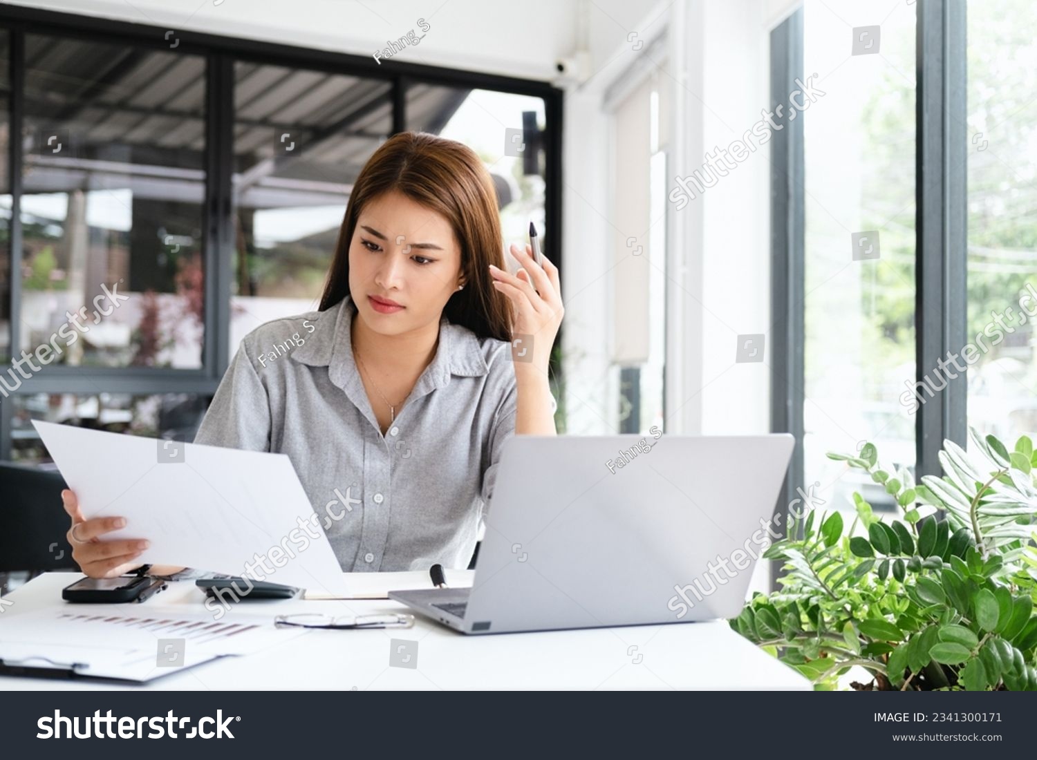 Young thoughtful Asian business woman executive manager wearing shirt working in modern office, taking notes and thinking of professional plan, project management, considering new business ideas. #2341300171