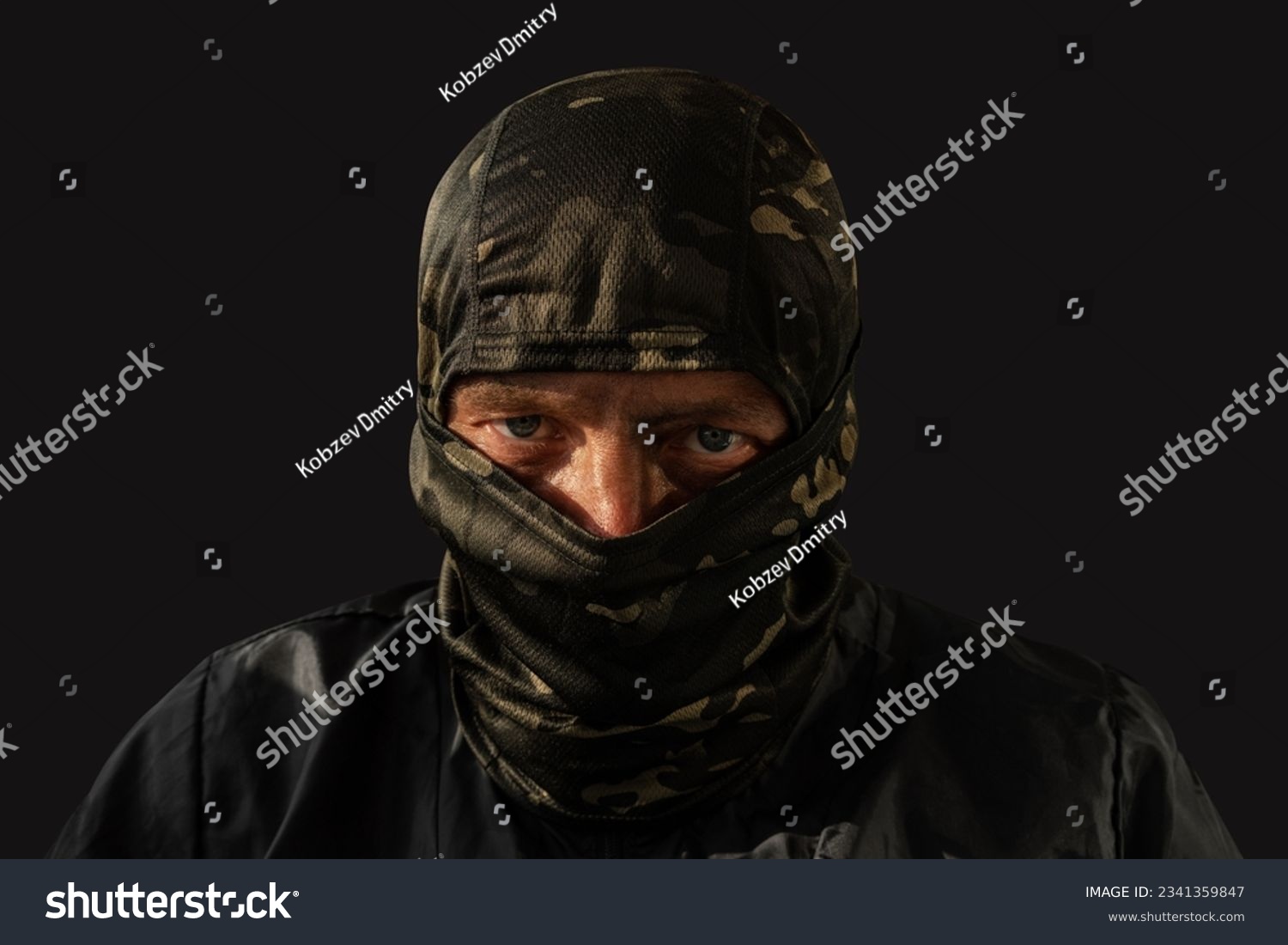 Military man with a dirty face and a camouflage mask. The concept of a man after military action or fraud, robbery. Closeup. Human on a dark background. #2341359847