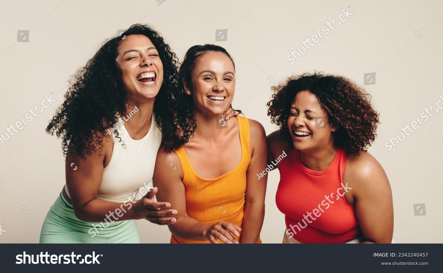 Cheerful group of three young, diverse female athletes celebrate their friendship and healthy lifestyle while wearing fitness clothing in a studio. Sporty young women laughing together. #2342240457