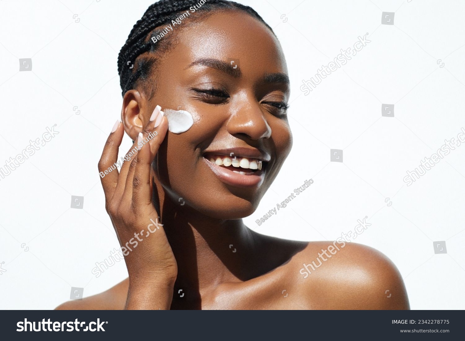 Beauty and skin care. Skincare hydration and oil balance. Portrait of African American woman with afro braids hairstyle is applying a cream smear on her face and standing against white background #2342278775