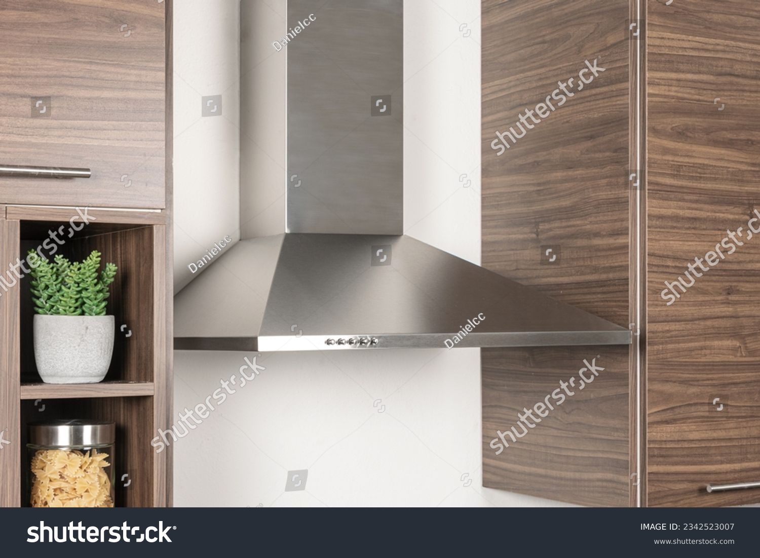 A Stainless Steel kitchen hood beside a melamine wooden kitchen cupboard set in the corner of a room, close up #2342523007
