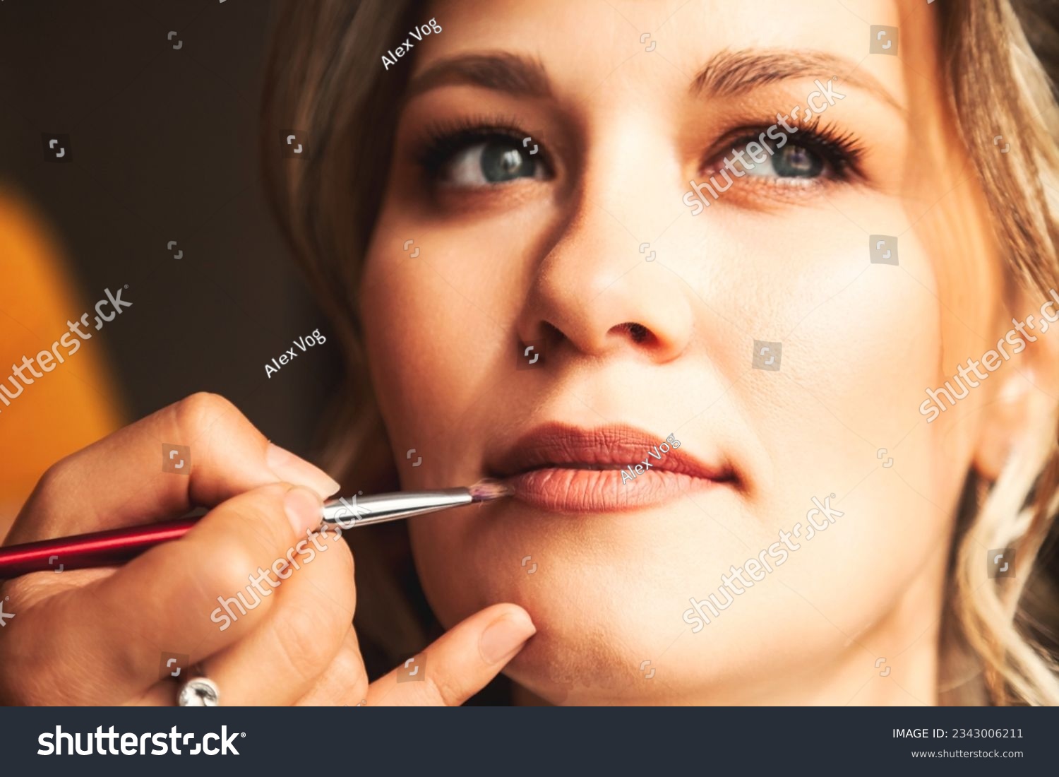 Visagiste make makeup for lovely lady bride at wedding day in hotel room. Close-up of make-up artist with lips brush doing wedding makeup for woman. Concept of luxury wed service. Copy ad text space #2343006211