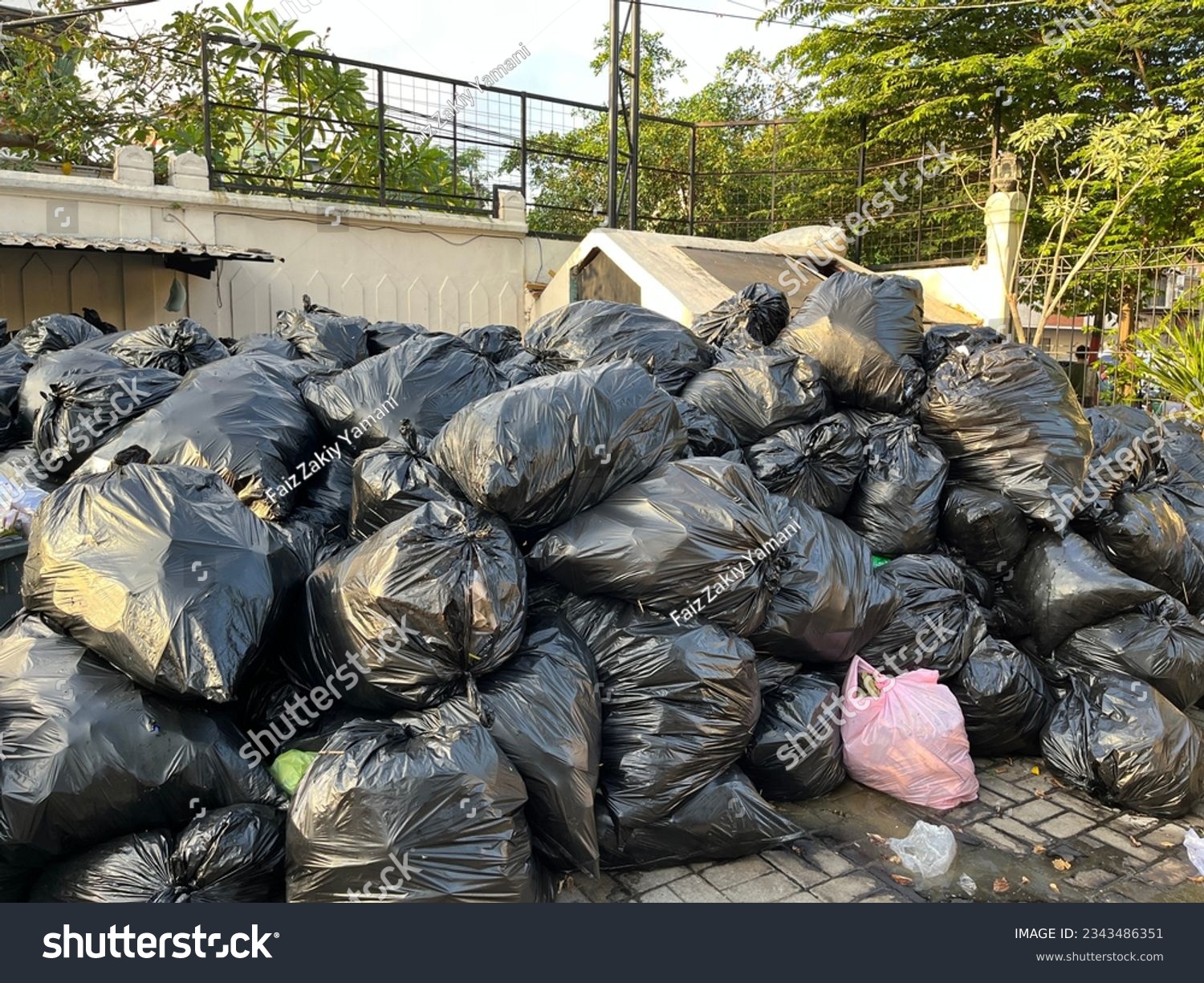 Overloaded dumping ground with pile of black garbage bags on the street  #2343486351