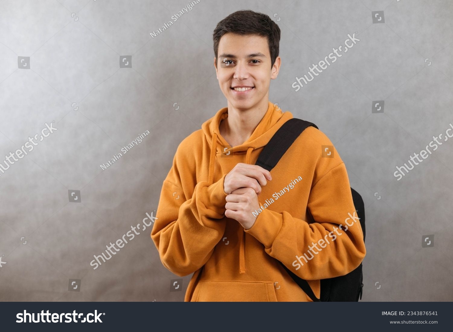 Portrait of a young student with a school bag. The teenager smiles and looks at the camera. A happy teenage boy on a grey background #2343876541