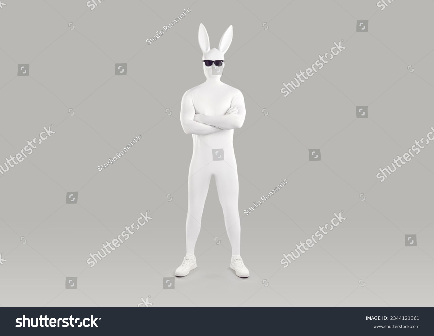 Full length portrait of faceless unrecognizable person in white spandex costume, hare mask with long ears and black glasses. Incognito funny man in bodysuit with crossed arms on grey background. #2344121361