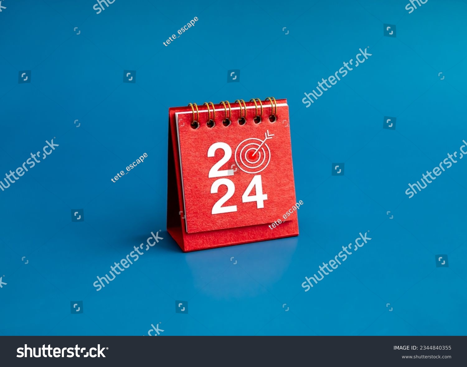 Happy new year 2024 banner background. 2024 numbers year with target dart icon on red small desk calendar cover standing on blue background, minimal style. Business goals plan and success concepts. #2344840355