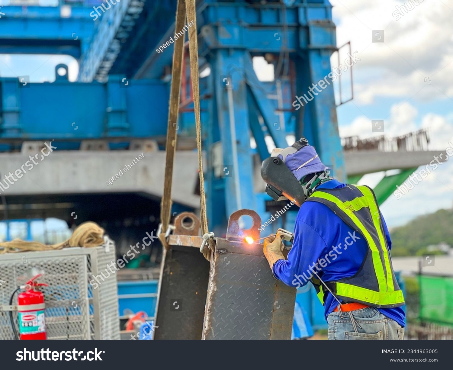 welder in blue suit Wearing a welding mask, welding steel at a construction site #2344963005