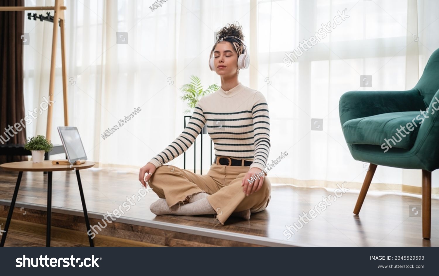 one woman adult caucasian female millennial using headphones for online guided meditation practicing mindfulness yoga with eyes closed on the floor at home real people self care concept copy space #2345529593