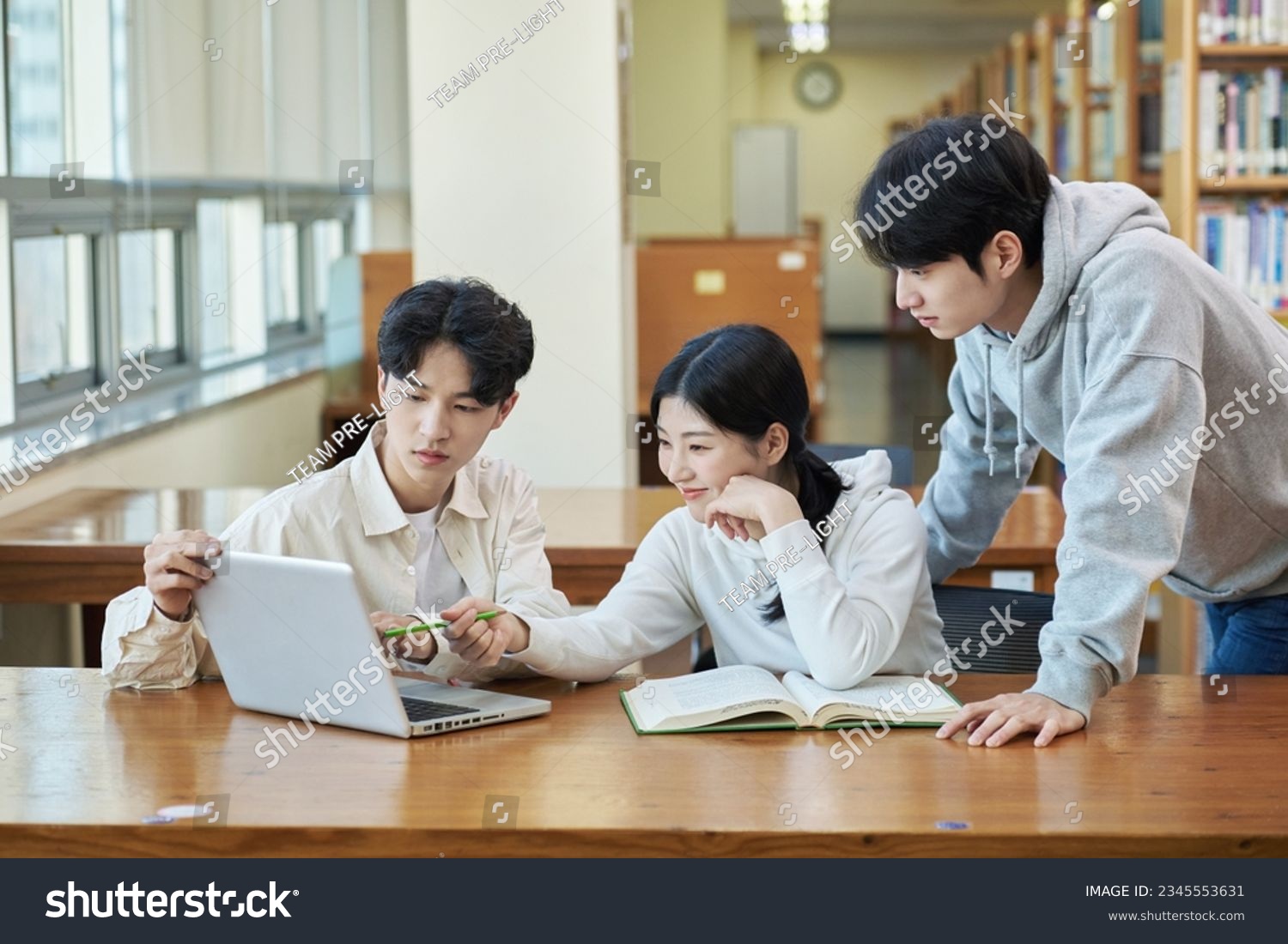 three young college student man and woman couple model and solo male model looking at laptop and book together in library of Asian Korean university #2345553631