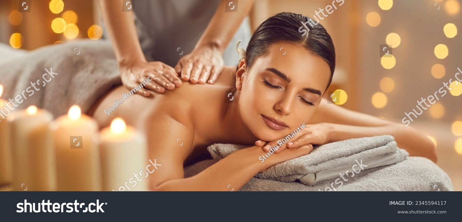 Beautiful young woman enjoying massage in spa salon. Relaxed brunette girl lying on massage bed with closed eyes during spa treatment procedure. Beauty treatment, skin care, wellbeing #2345594117