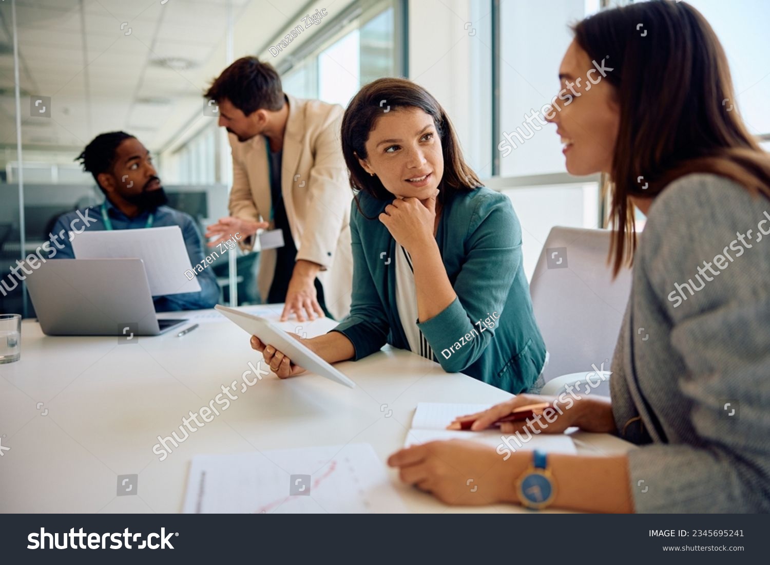 Mid adult businesswoman using digital tablet while talking to female coworker on a meeting in the office.  #2345695241