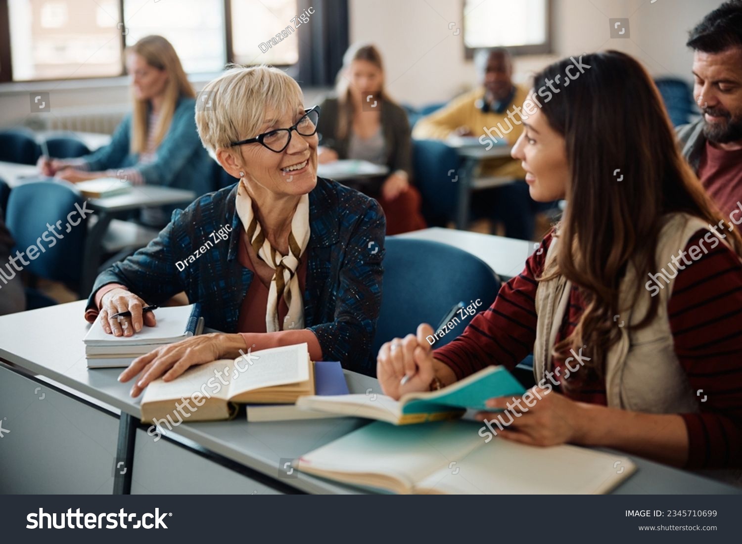Smiling female adult learners communicating during a class in lecture hall. Focus is on mature woman.  #2345710699