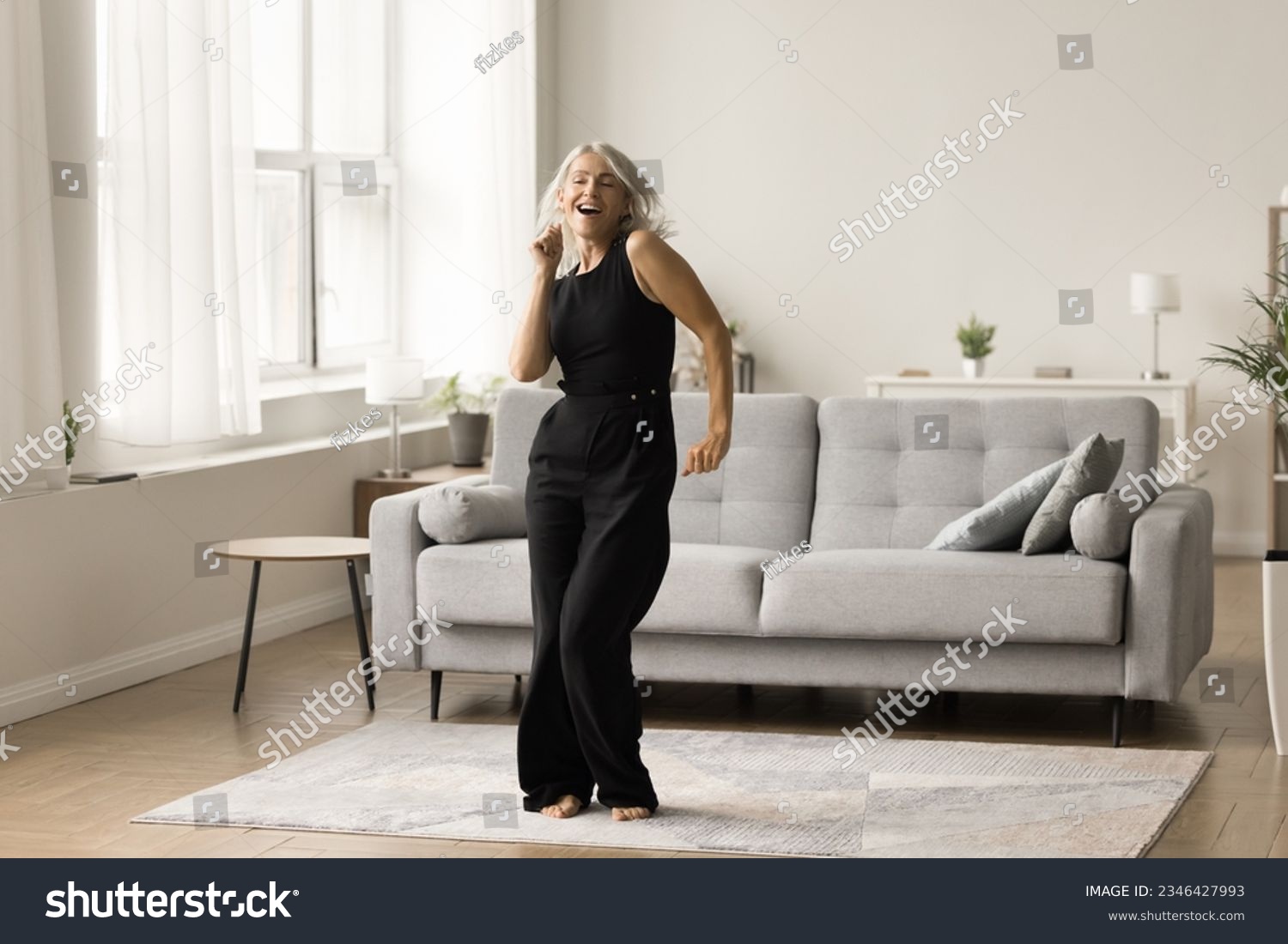 Joyful active senior lady excited with single dance at home enjoying motion, activity, music, singing song, having fun in cozy comfortable living room interior. Full length wide shot #2346427993