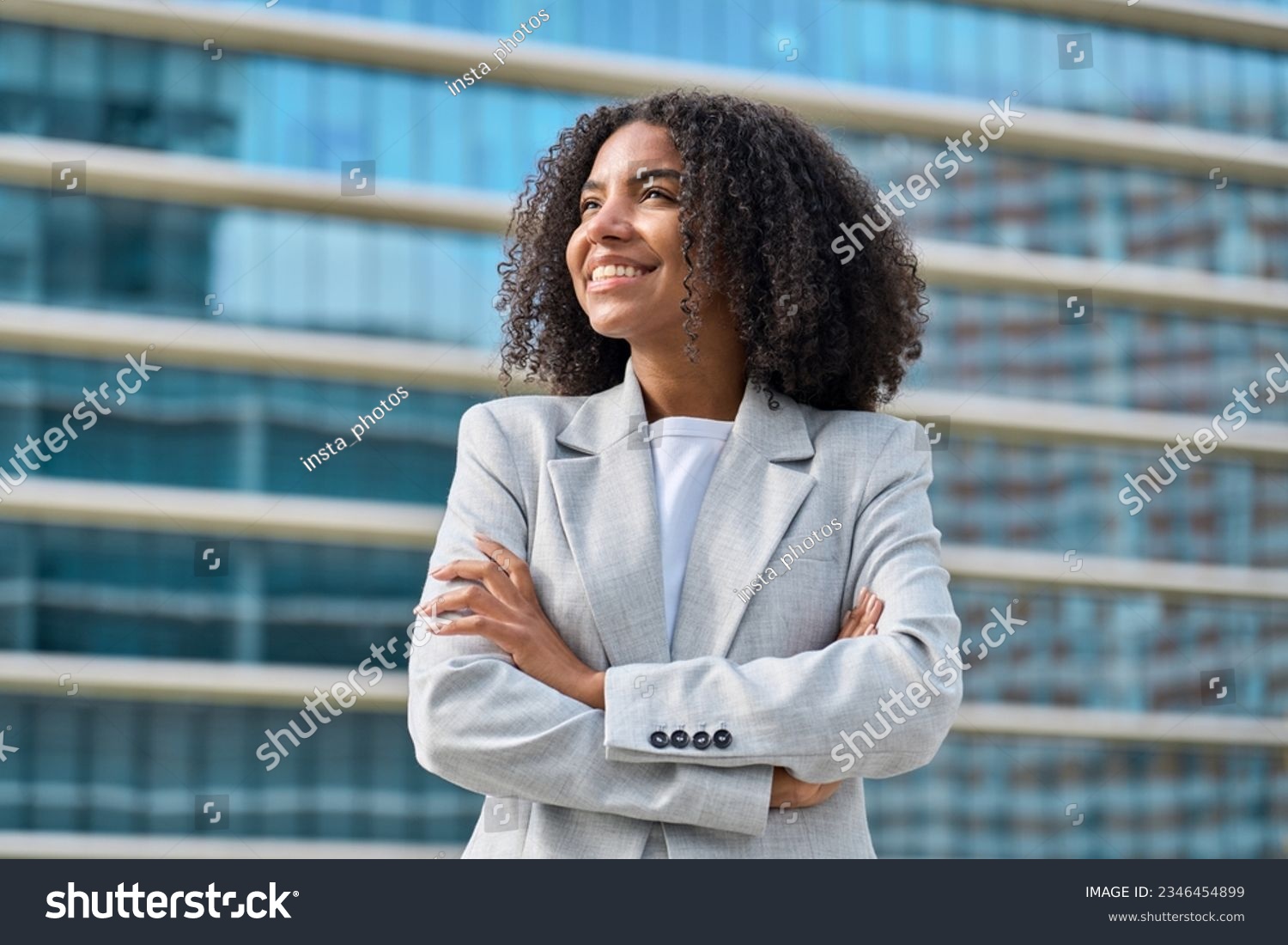 Happy young African American business woman standing in city looking away. Confident smiling confident professional businesswoman leader wearing suit thinking of success, dreaming of new goal outdoor. #2346454899