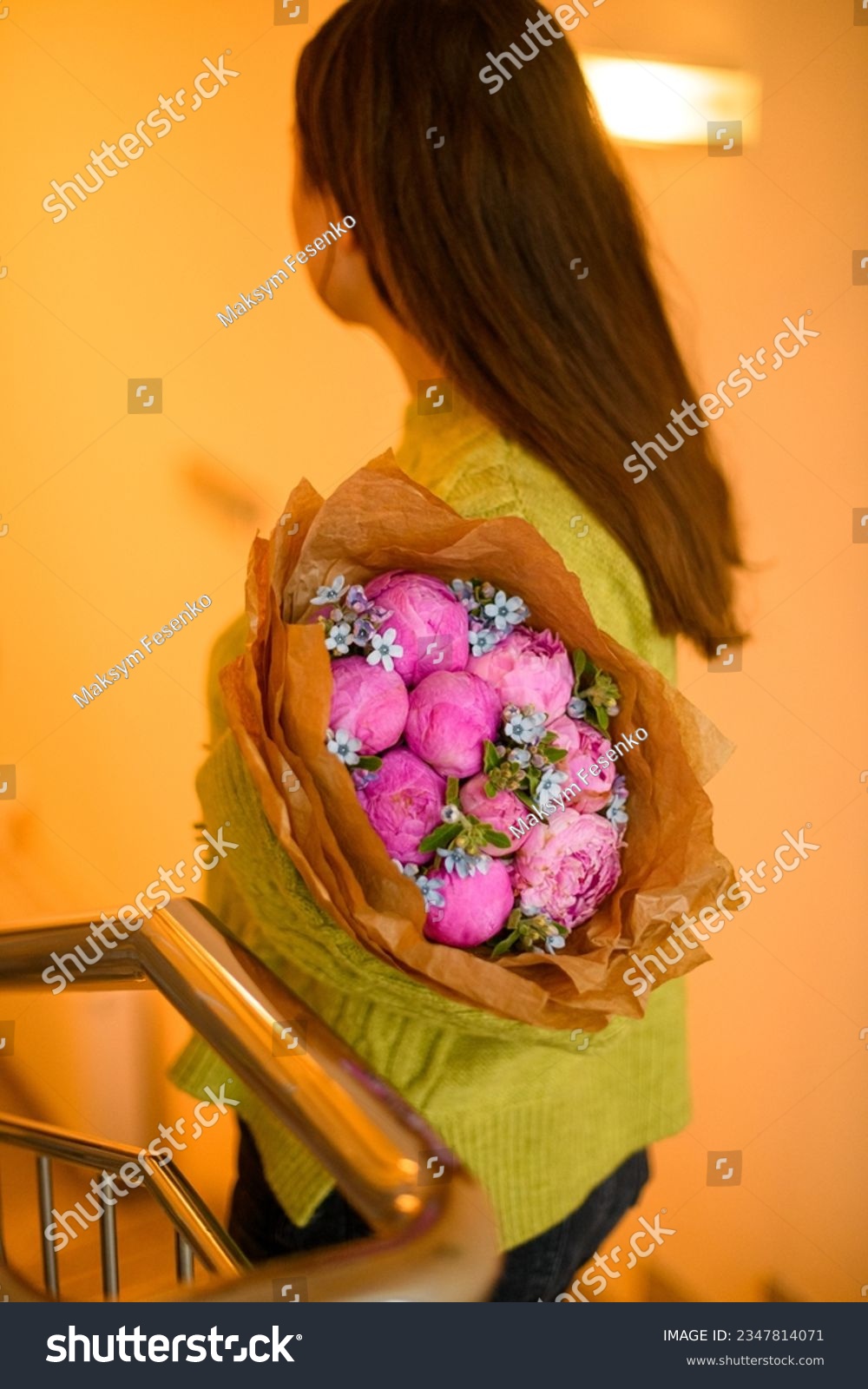Young beautiful darkhair woman in green sweater posing with luxury bouquet of fresh pink peonies in stairwell interior #2347814071