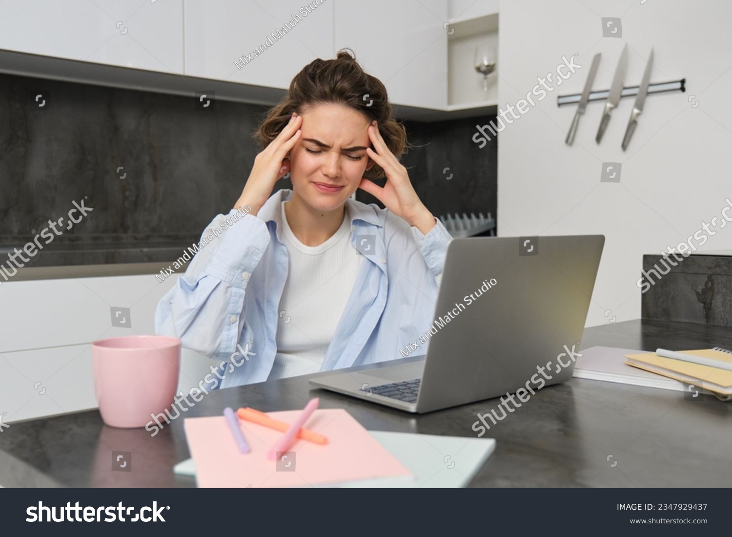 Woman has headache while works from home. Girl has painful migraine, sits near laptop, grimaces from discomfort. #2347929437