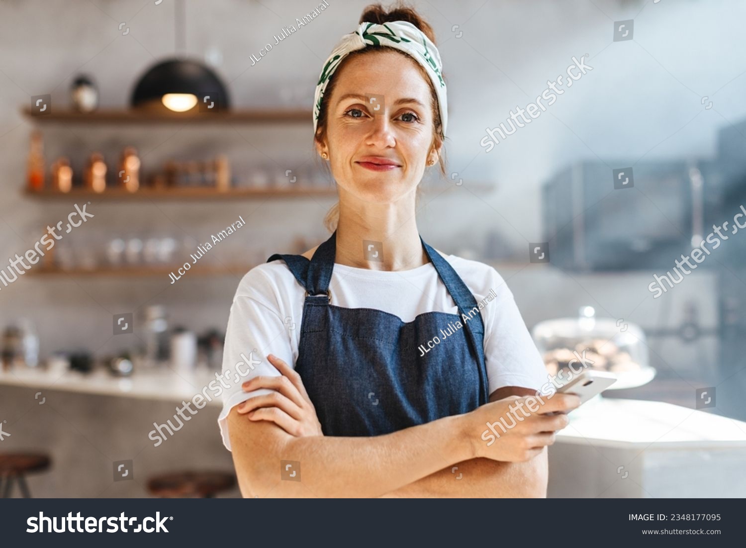 Caucasian coffee shop owner standing in her establishment, embracing technology with her smartphone and using it to streamline operations and provide a modern, efficient experience for her customers. #2348177095