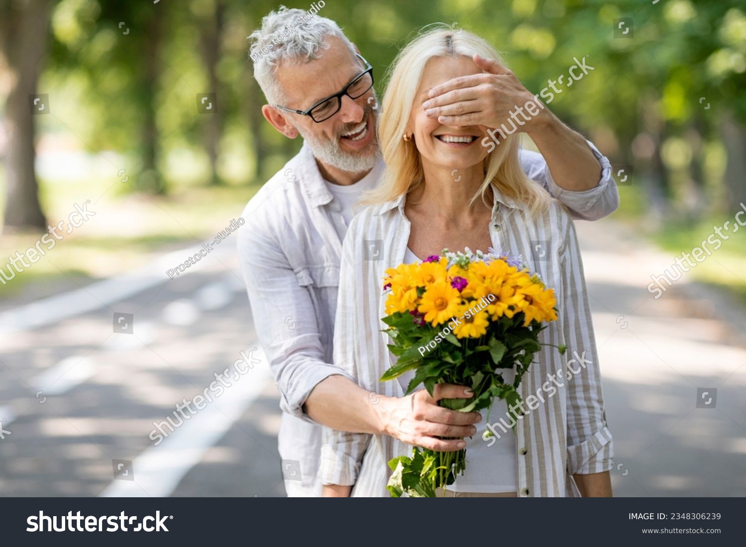 Loving Mature Husband Surprising Wife With Flowers, Covering Her Eyes And Giving Bouquet, Caring Man Greeting Spouse With Anniversary Or Making Romantic Surprise During Outdoor Date In Park #2348306239