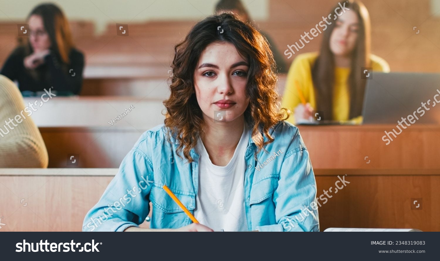 Close up of young pretty Caucasian female student sitting at desk in auditorium and reading textbook. College education concept. Girl read book at lection in University. Obtaining knowledge. #2348319083