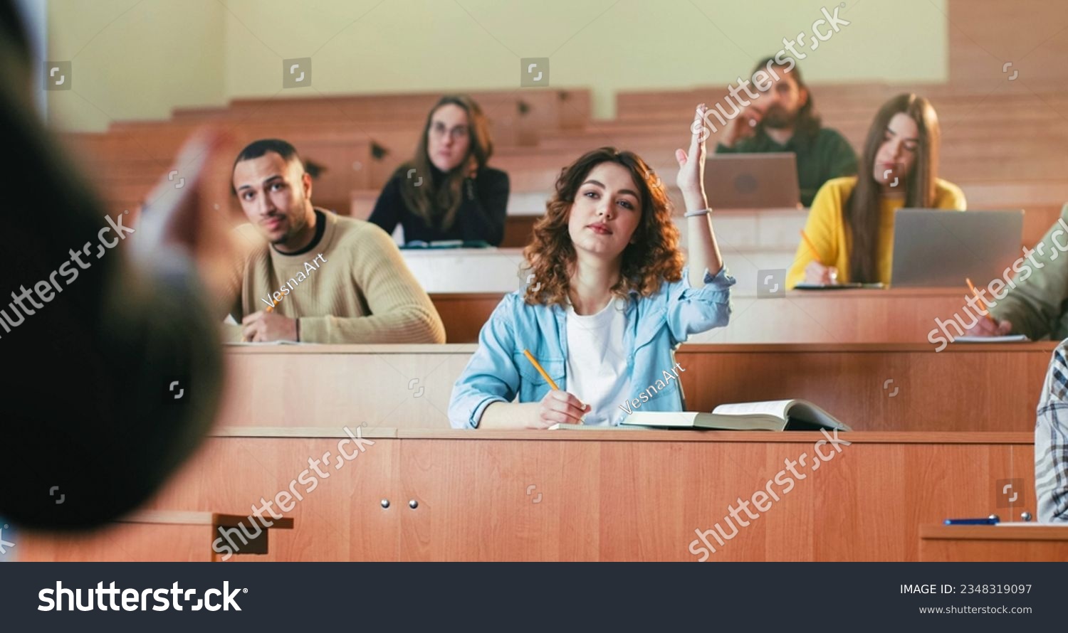 Portrait of young beautiful Caucasian female student sitting at the desk, noting lection and looking at camera. Indoor in classroom. High school concept. Girl studying at University and writing down. #2348319097