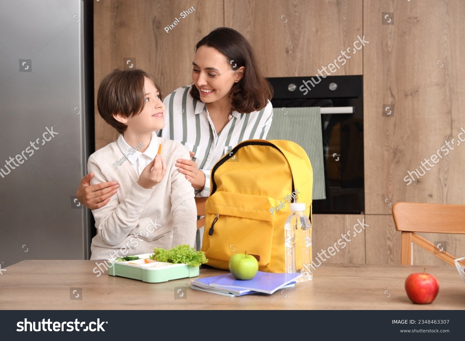 Mother helping her little son to pack schoolbag and lunch in kitchen #2348463307