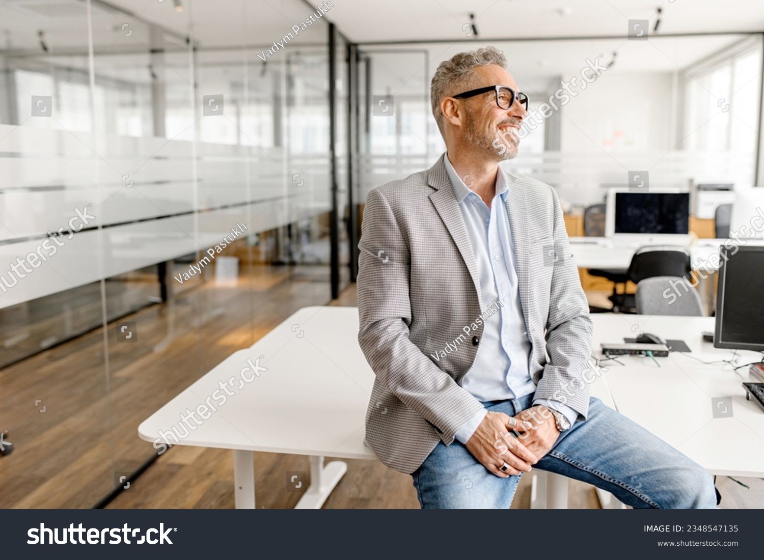 Serene modern middle aged businessman in formal wear leaned on the desk looking away, inspired and calm mature business owner at the office, confident grey-haired man in relaxed pose #2348547135