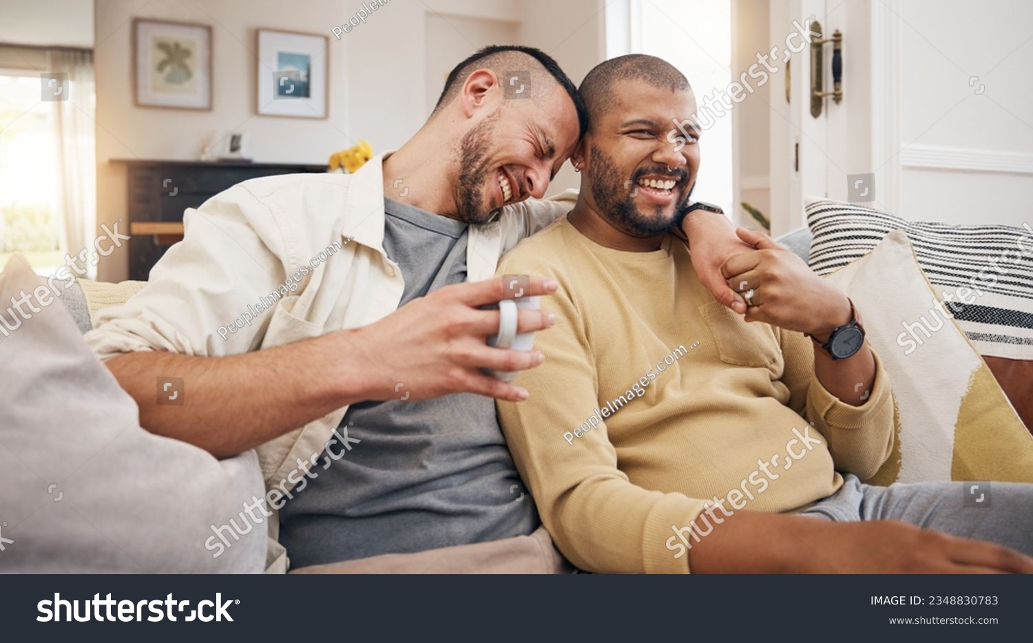 Laughing, relax and a gay couple on the sofa with coffee, conversation or love in a house. Happy, together and lgbt men on the living room couch for a funny story, communication or speaking with tea #2348830783