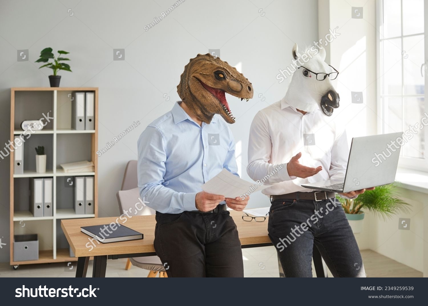 Funny animal people use computer at work. Team of 2 men in unusual masquerade dinosaur and horse masks standing by desk in office workplace, preparing creative business presentation on laptop device #2349259539