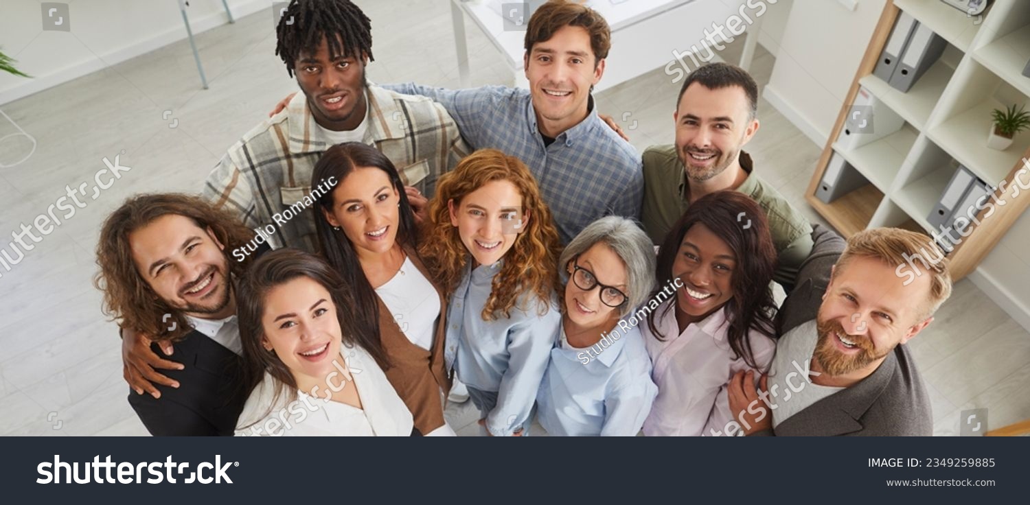 Happy diverse business team at work in office. Top view high angle shot from above group portrait of young and senior multiracial multiethnic people standing together, looking up at camera and smiling #2349259885