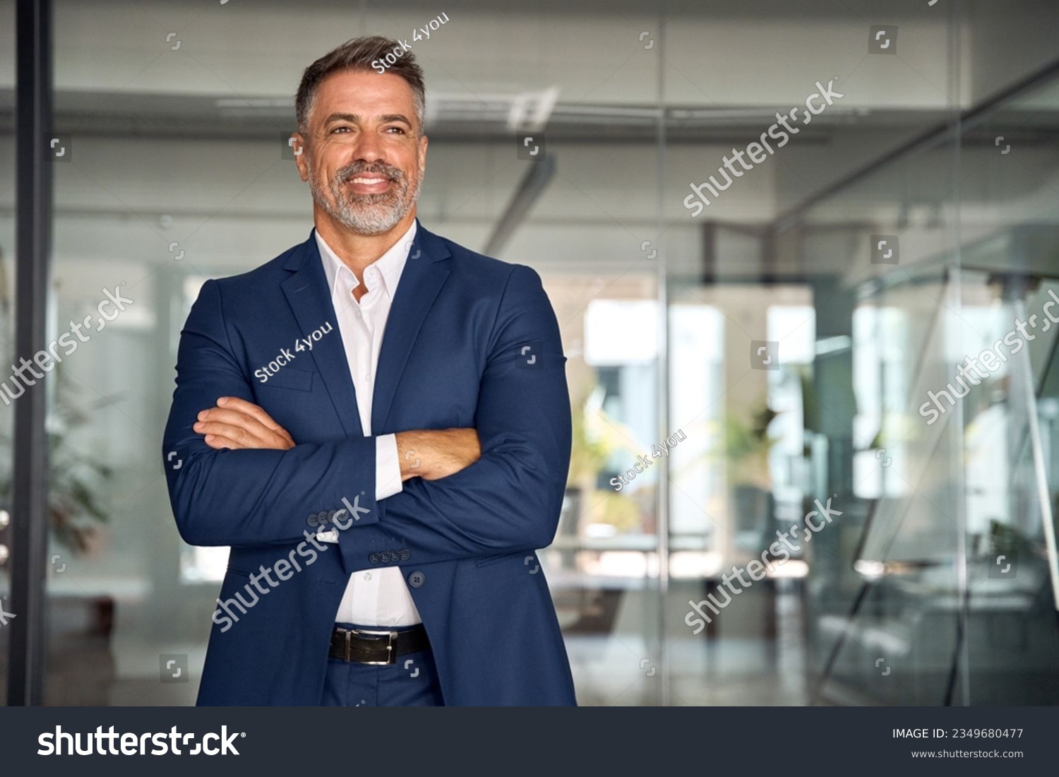 Handsome hispanic senior business man with crossed arms smiling aside. Indian or latin confident mature good looking middle age leader male businessman on blur office background with copy space. #2349680477