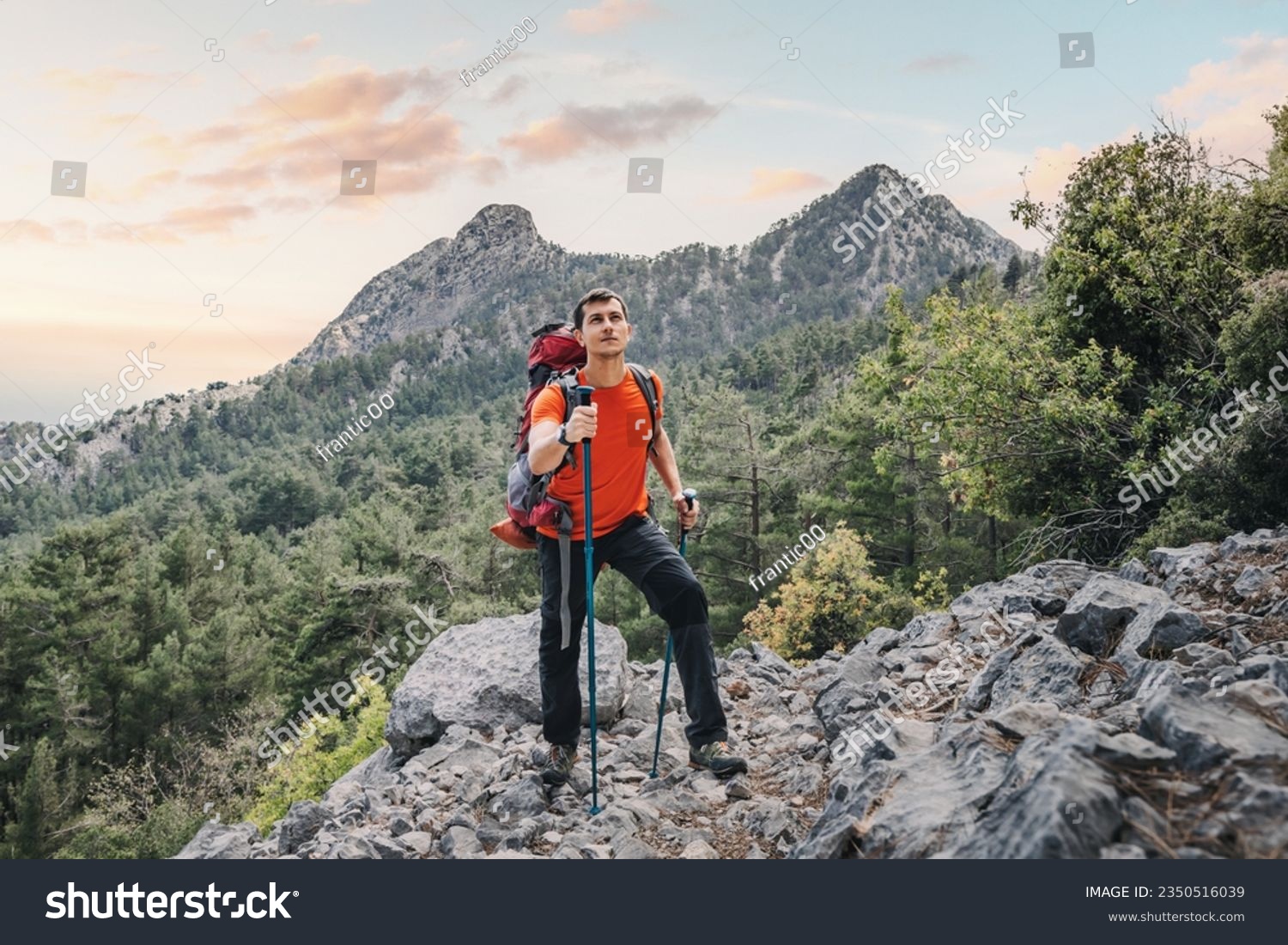 Happy hiker man with trekking backpack and hiking poles on a rocky cliff during walk on Lycian Way trail in turkish mountains #2350516039