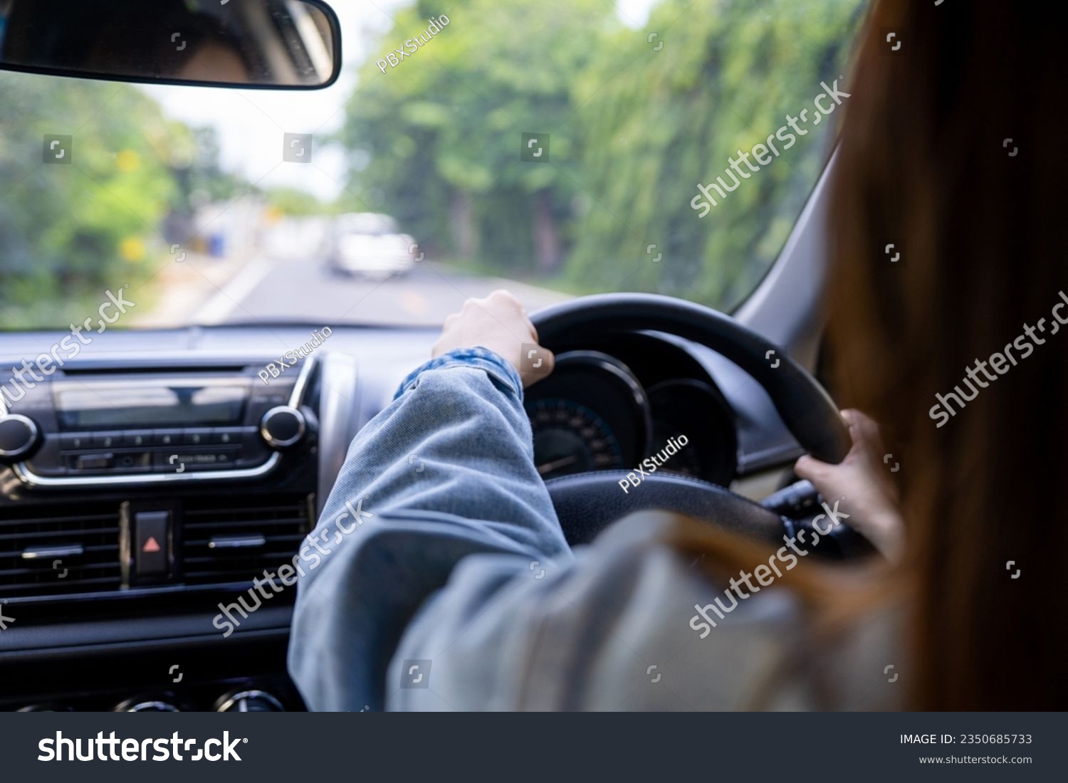 Back view of a woman driving car for summer road trip travel. Driver hand holding steering wheel for control car. Safe driving concept. #2350685733
