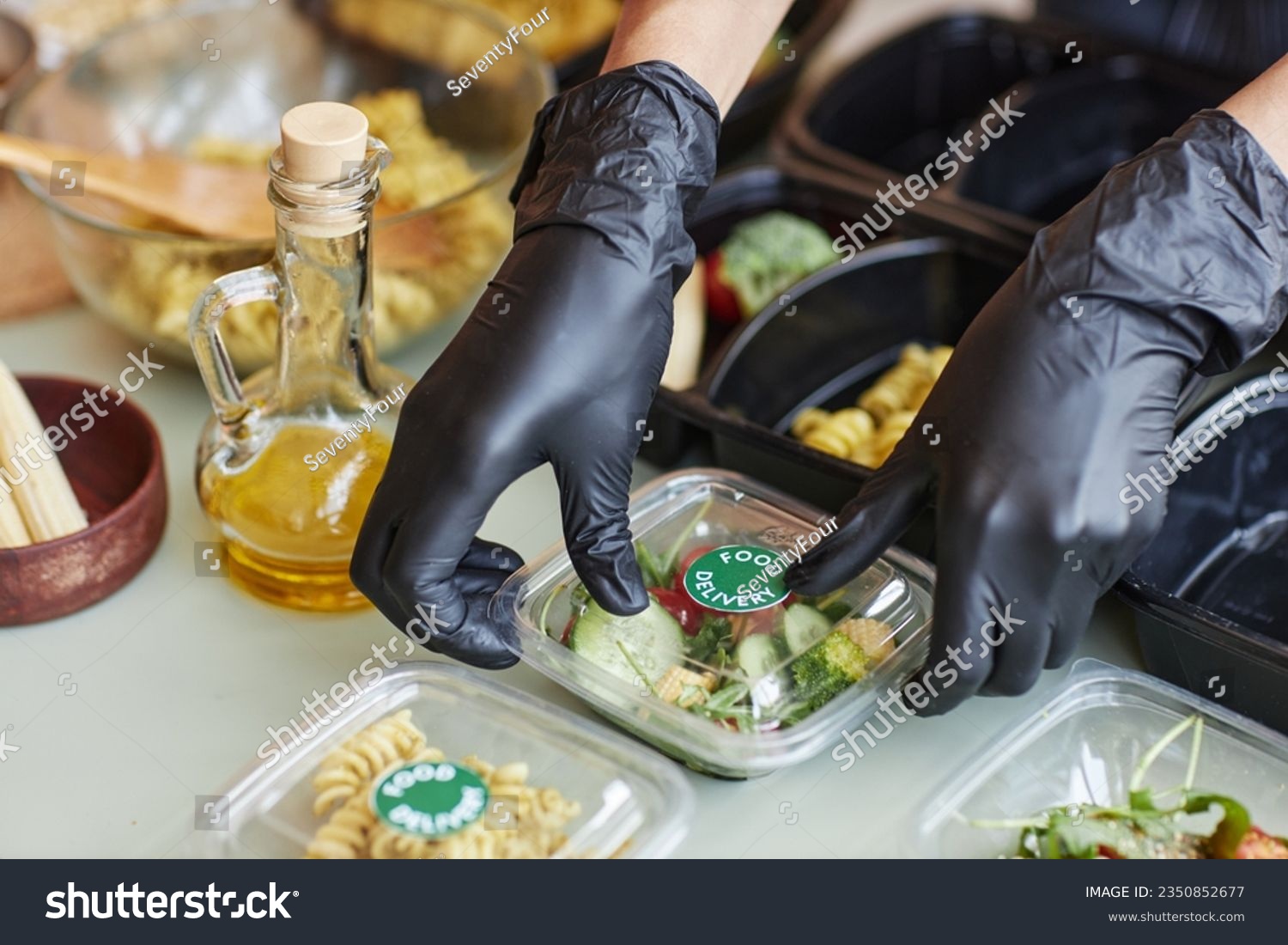Close up of cafe worker wearing gloves packing food delivery order with salad, copy space #2350852677