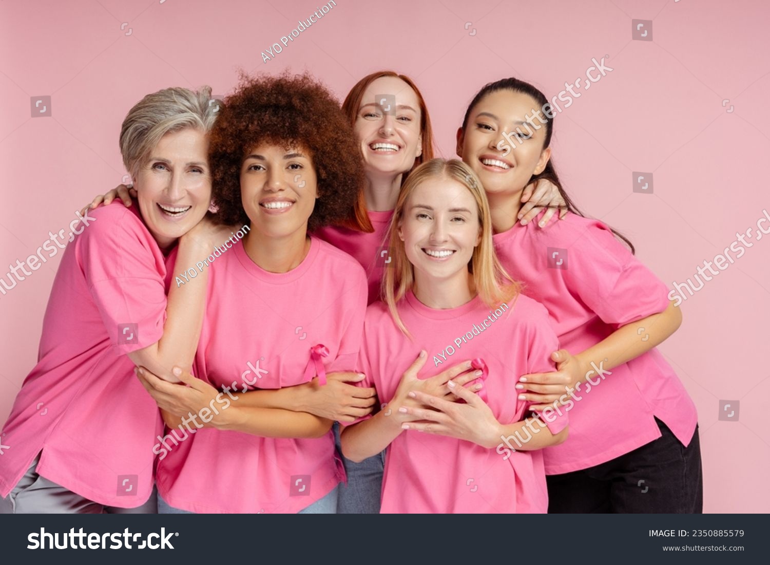 Group of smiling confident multiracial women wearing t shirts with pink ribbon looking at camera isolated on pink background. Health care, support, prevention. Breast cancer awareness month concept #2350885579