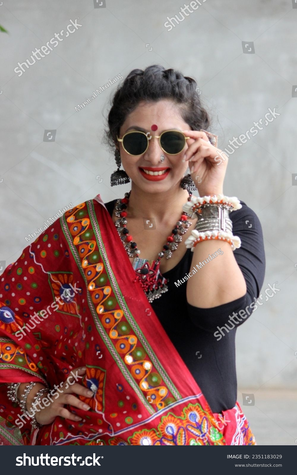 Indian woman in a stylish traditional look for Navratri for playing Garba and dandiya wirh sun glasses and fabric and oxidized jewelry. red and black outfit with traitional bangles earings, bindi. #2351183029