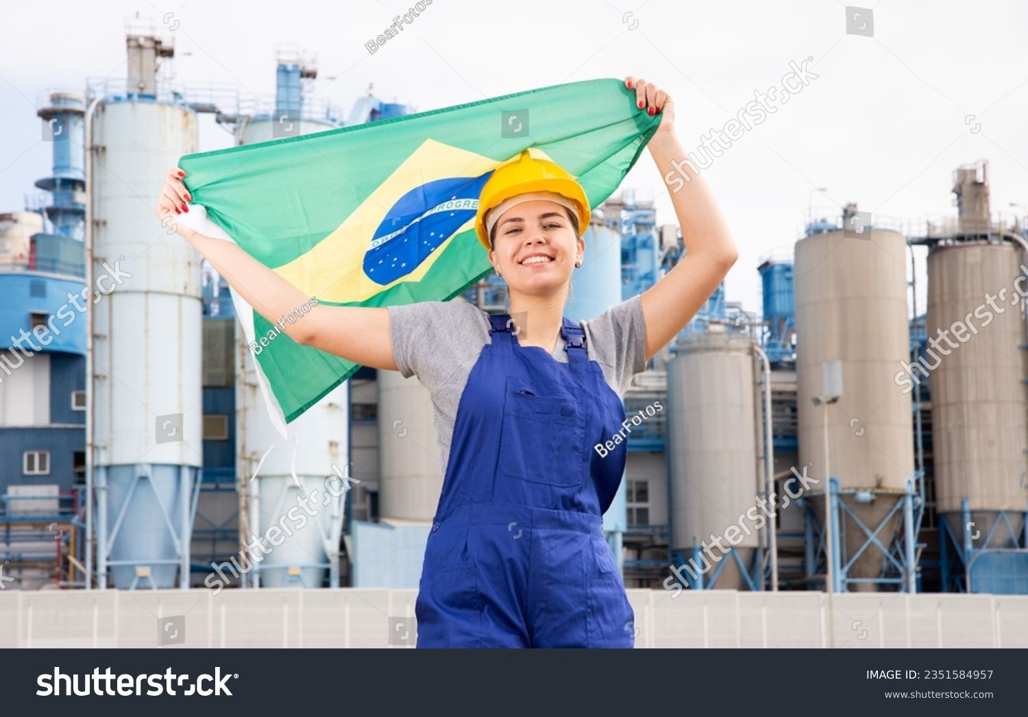 Cheerful female worker in hardhat with brazilian flag standing in front of factory #2351584957