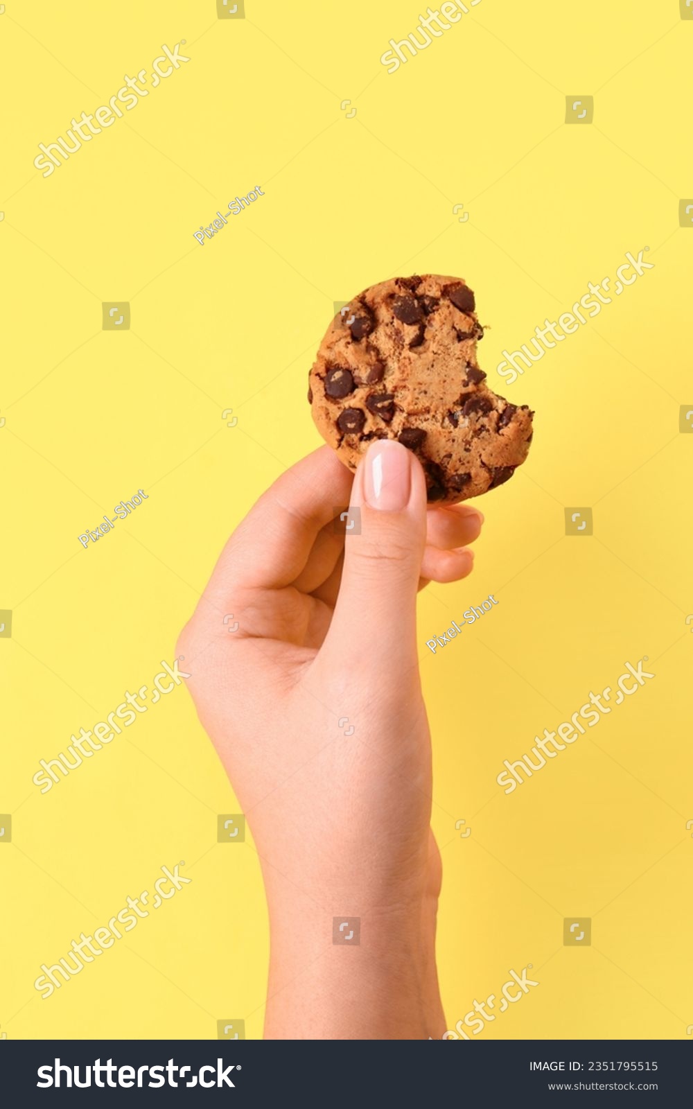Woman holding bitten cookie with chocolate chips on yellow background #2351795515