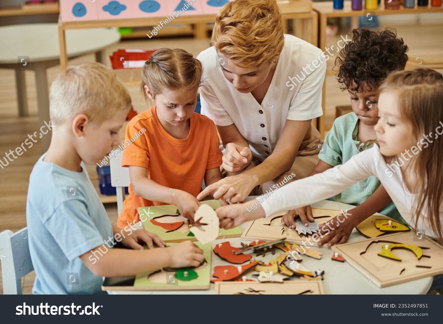 teacher playing with interracial children with didactic materials in montessori school #2352497851