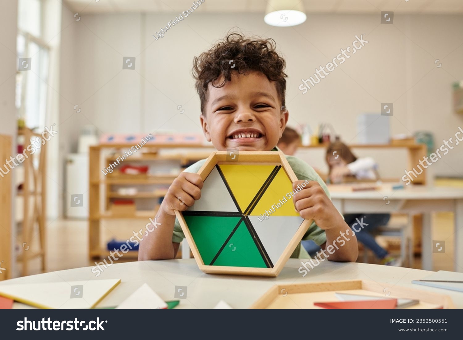 positive african american boy holding wooden didactic materials in blurred montessori school #2352500551