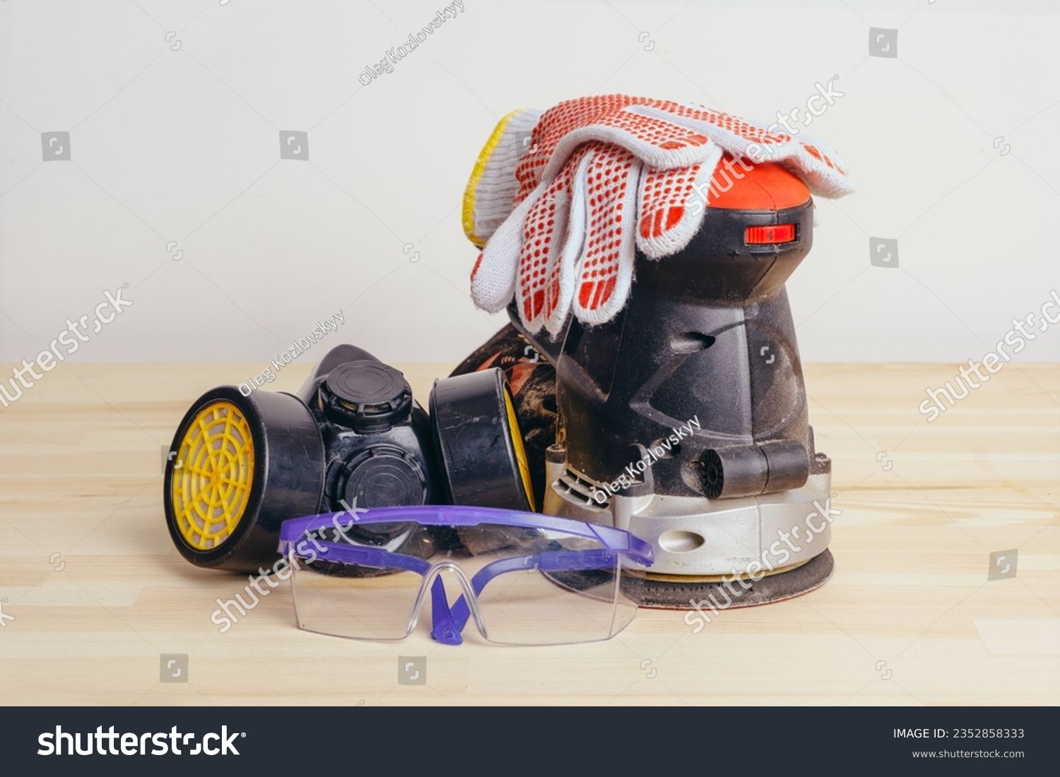 Grinding machine, gloves, goggles and a protective mask on a wooden table against a white wall. #2352858333