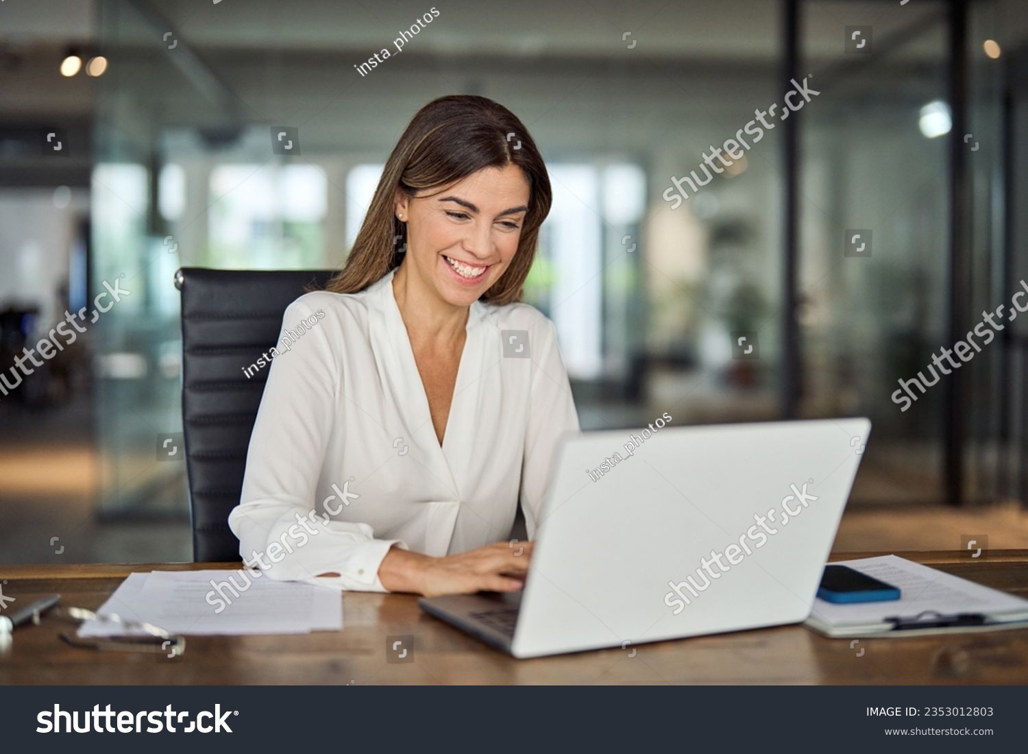 Happy cheerful mid aged business woman executive in office using laptop at work, smiling professional mature 40 years old female company manager working on computer at workplace. #2353012803