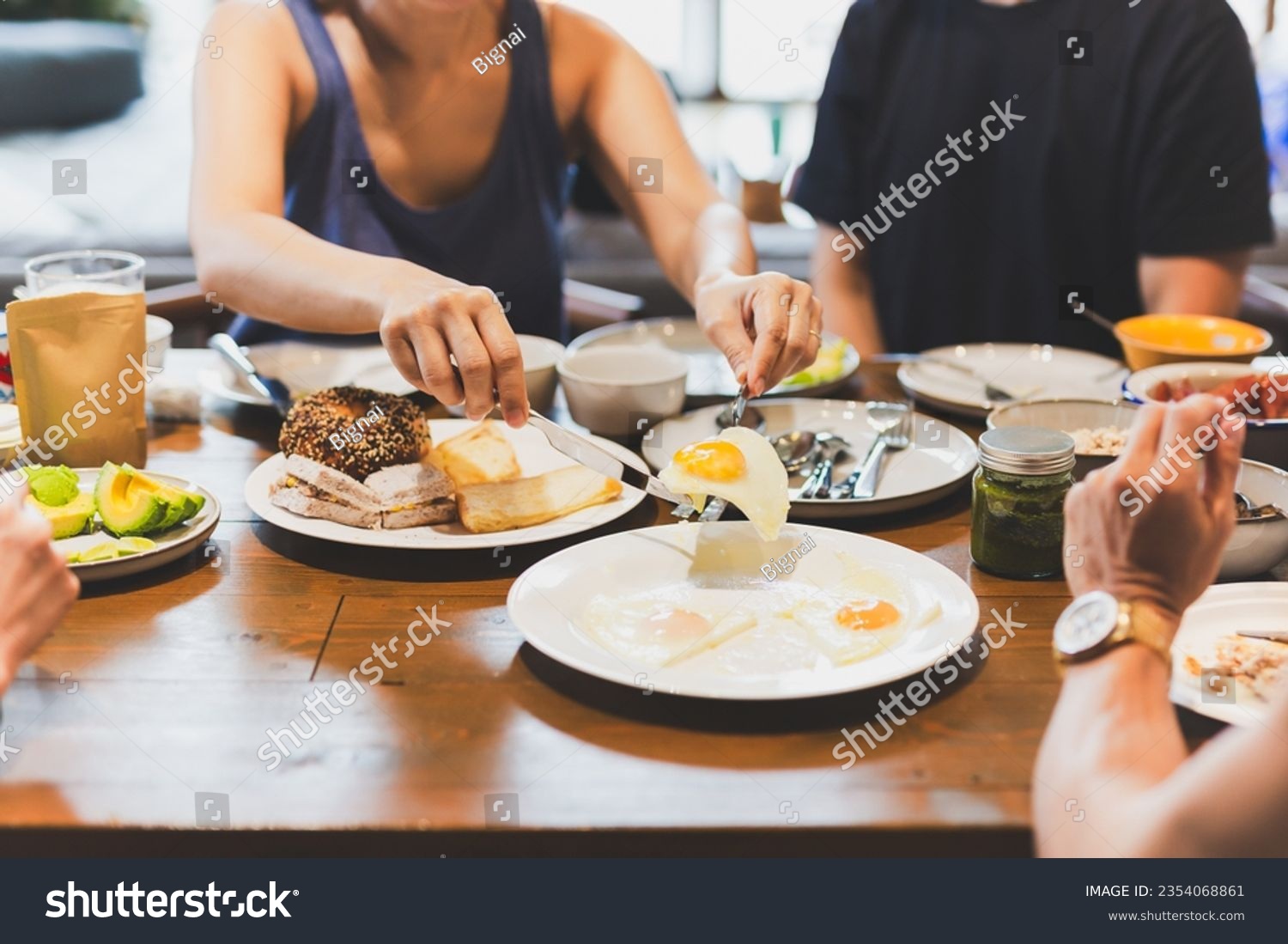 Woman eating fried eggs breakfast with friends on wooden table #2354068861
