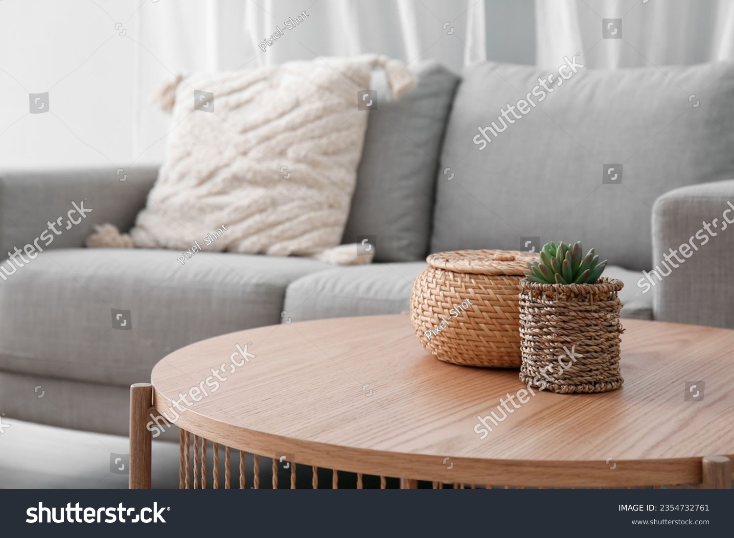 Wooden coffee table with with houseplant and wicker basket near grey sofa in living room #2354732761
