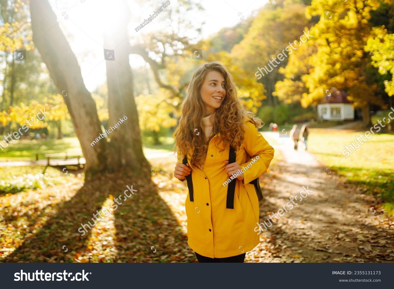 Happy female hiker in yellow coat walking in golden autumn forest. Beautiful woman has fun in autumn in the park. Trips. Active lifestyle. #2355131173