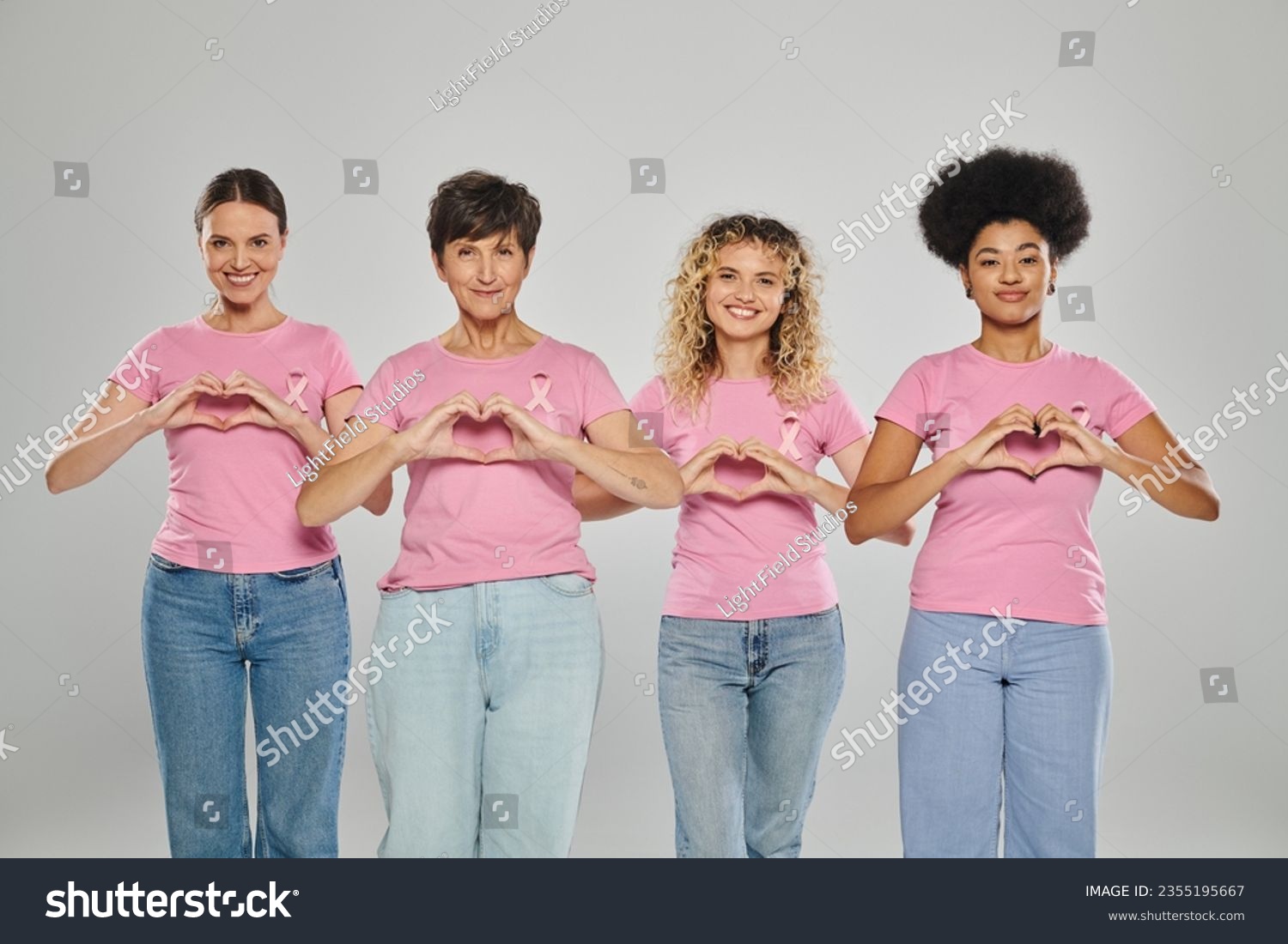 breast cancer awareness, happy interracial women with pink ribbons showing heart on grey, diversity #2355195667
