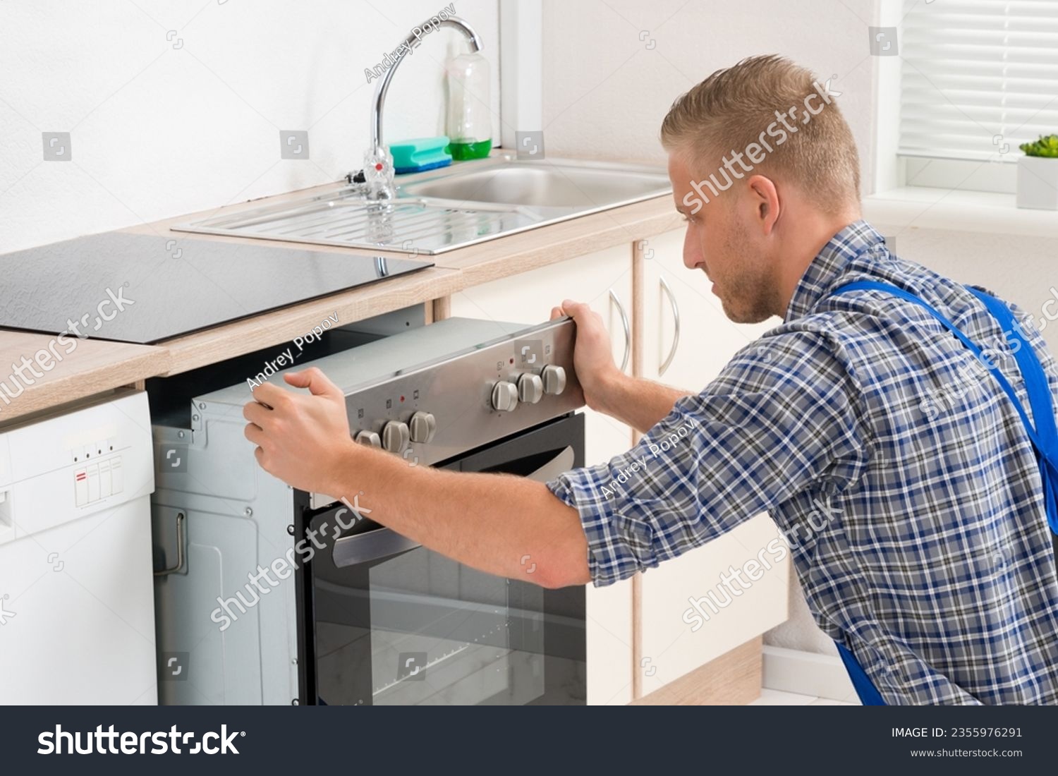 Young Repairman In Overall Repairing Oven In Kitchen #2355976291