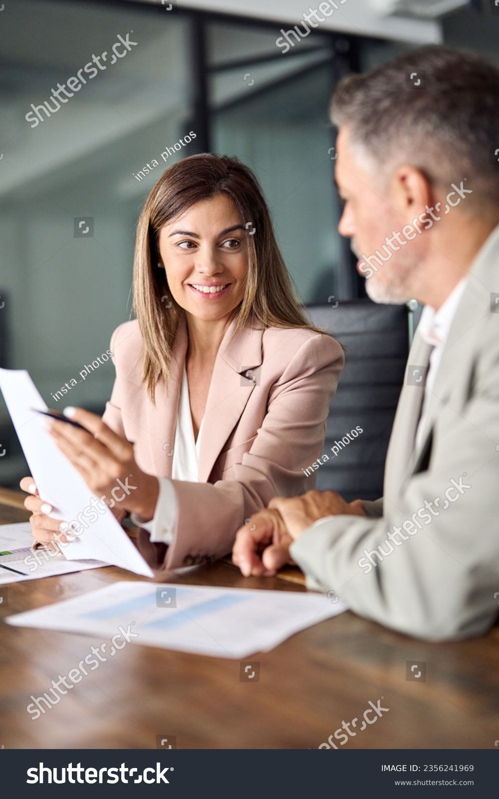 Female lawyer or financial advisor consulting older male client investor showing documents at meeting. Two mature business executive colleagues discussing account paperwork report in office. Vertical #2356241969