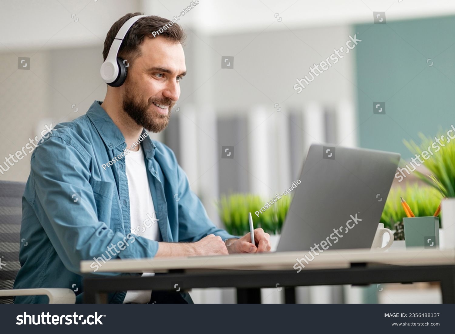 Online Education. Smiling Young Man Wearing Wireless Headphones Using Laptiop And Taking Notes, Handsome Millennial Male Watching Webinar, Attending Internet Lesson, Sitting At Desk At Office #2356488137